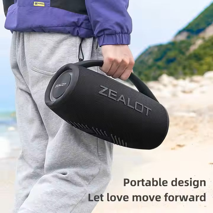 Person holding a black Zealot portable speaker on a beach with scenic background
