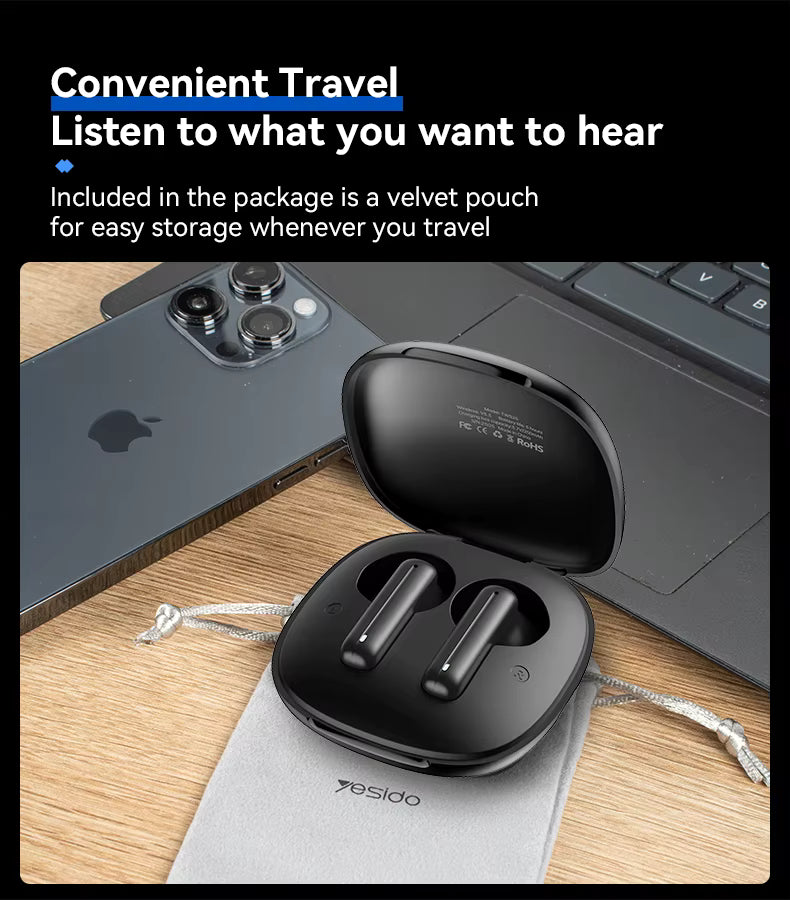 Black wireless earbuds in a case with a laptop and phone on a wooden surface