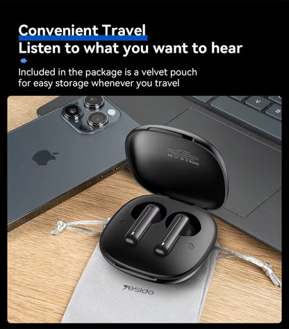 Black wireless earbuds in a case with a laptop and phone on a wooden surface